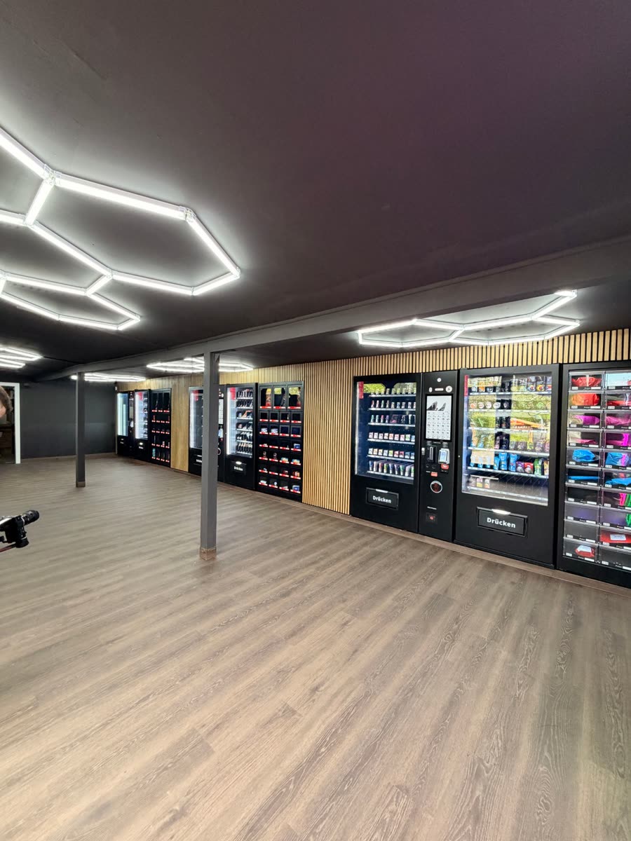 24SEVEN E-Kiosk Geyer nach dem Umbau — Automatenreihe mit Holzwand und LED-Beleuchtung